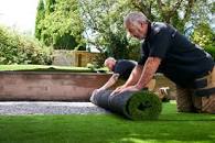 Rolling out and laying new artificial grass in a garden.