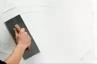 Plasterer holding a trowel plastering a wall.