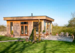 A wide view shot of a modern garden office on a bright summers day, a clear sky is above the wooden office and standing stones can be seen on the grass.
