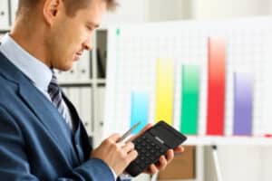 Male arm in suit hold calculator pressing buttons in office closeup. Electronic keypad math data invest credit debit research mortgage loan money saving payment economic debt school in loss assessing.