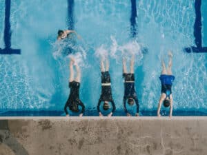 Aerial view directly above Asian chinese swimmer practicing leg splashing water at poolside guided by the swimming coach